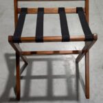 “Suporte de Malas para Hotéis em madeira, com quatro cintas resistentes, velatura média ou escura, barra de proteção de parede e estrutura dobrável para facilitar o uso da bagagem no quarto.”